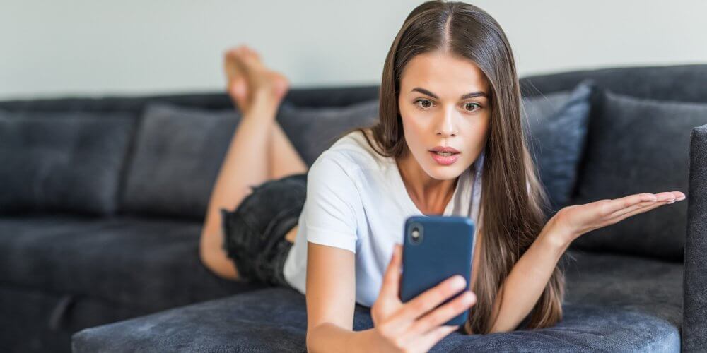 Zakłopotana kobieta leżąca na łóżku z telefonem